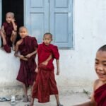 Cheerful young Buddhist novice monks playing outside a temple, wearing traditional robes.