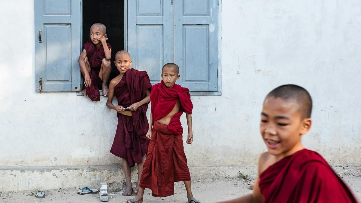 Cheerful young Buddhist novice monks playing outside a temple, wearing traditional robes.