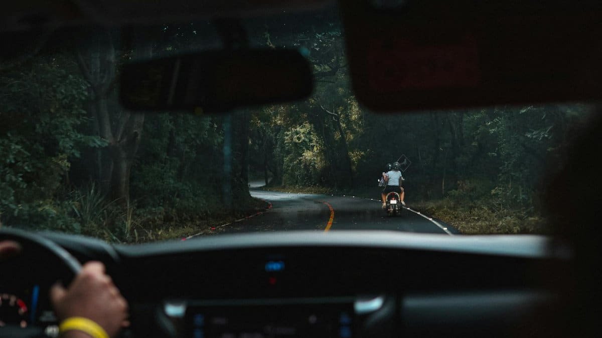 View from inside a car of a winding forest road in Nicaragua with a motorbike ahead.