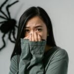 An anxious woman indoors with a large wall spider, depicting arachnophobia.