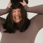 Young woman expressing frustration with hands on head in a studio shoot.