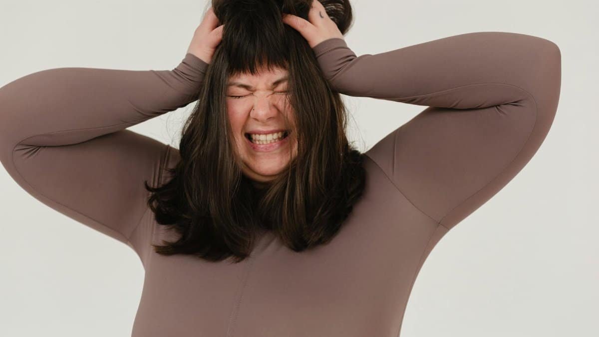Young woman expressing frustration with hands on head in a studio shoot.