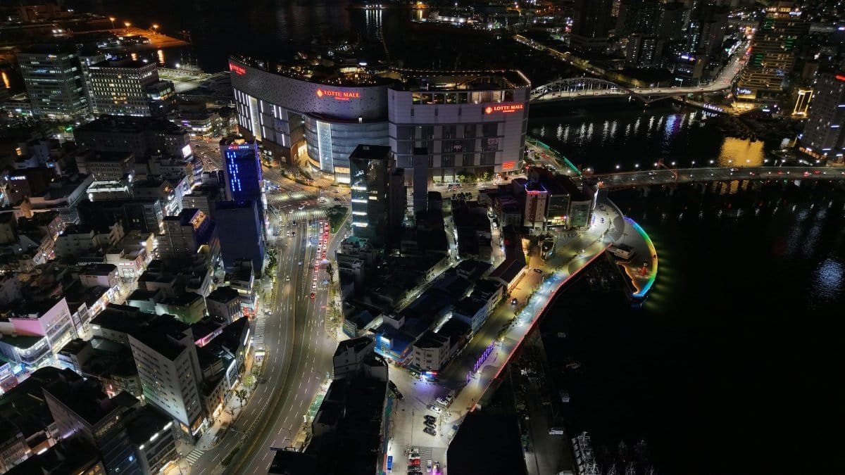 A stunning aerial shot of Busan, South Korea, featuring Lotte Mall and colorful city lights at night.