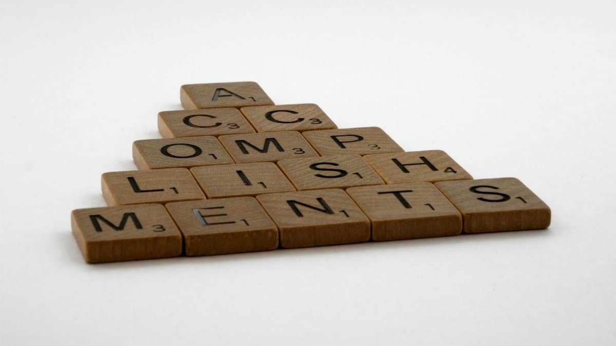 Wooden scrabble tiles forming the word 'accomplishments' on a white background.