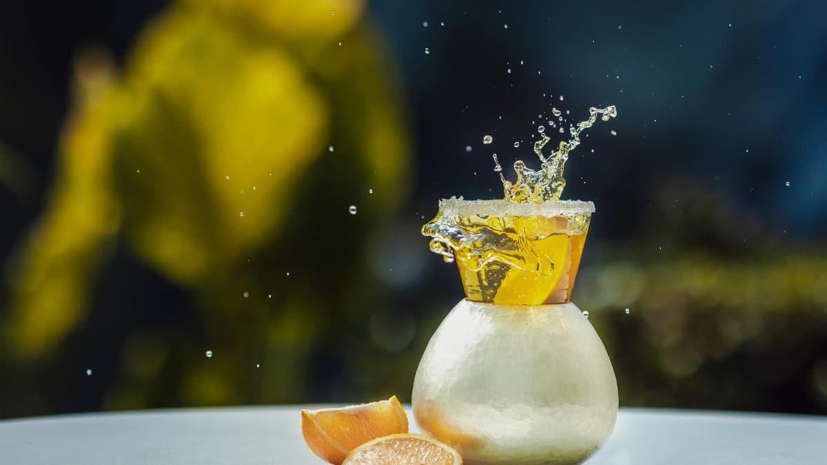 A vibrant splash of citrus beverage in a round glass with bright bokeh background for lively outdoor drinks theme.