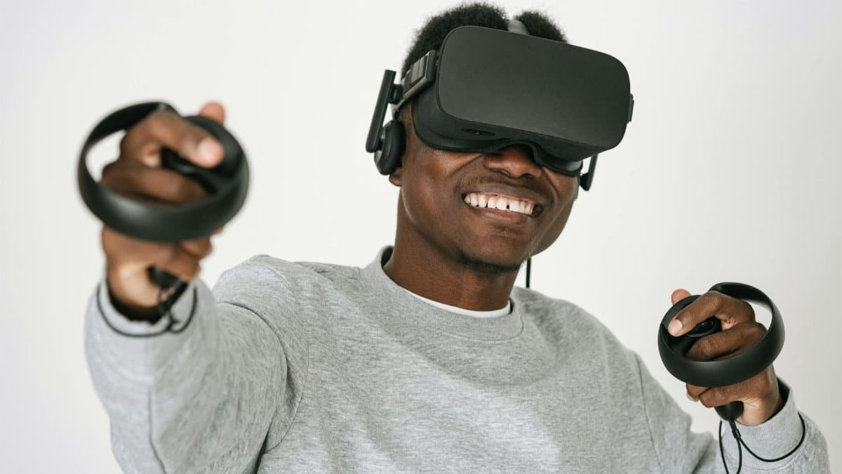 A man wearing a VR headset and controllers is smiling and enjoying a virtual reality experience indoors.