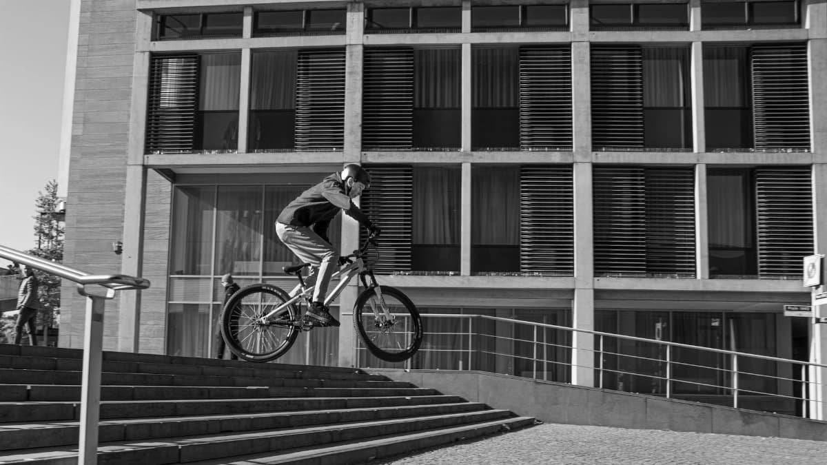 BMX rider performs a freestyle stunt on steps in urban Maastricht setting.