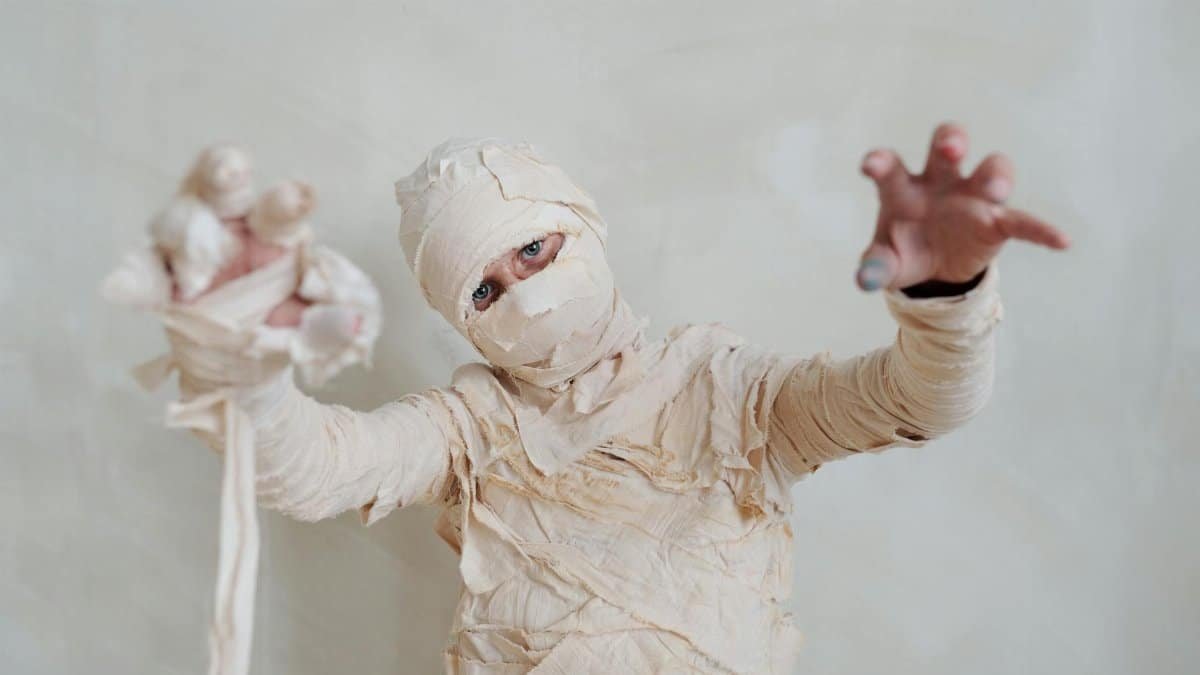 A child dressed as a mummy poses indoors for a spooky Halloween portrait.