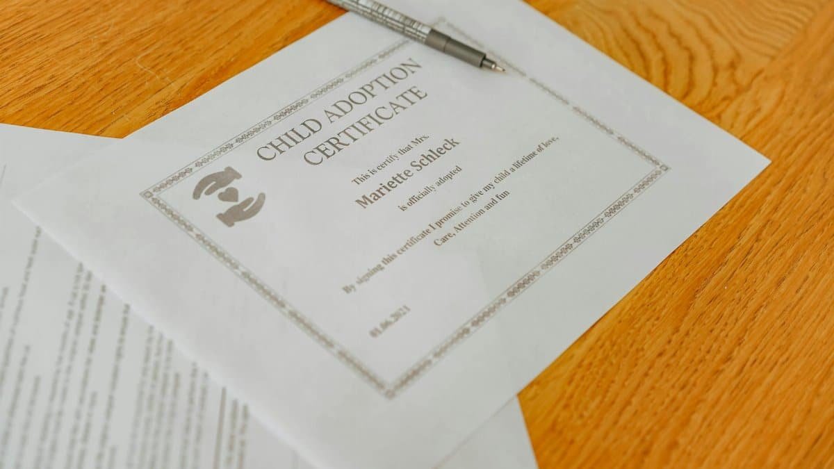 Close-up of a child adoption certificate and documents with a pen on a wooden table.