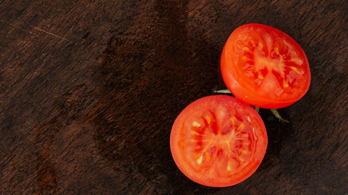 Top view of fresh ripe and juicy halves of tomato placed on dark brown wooden table