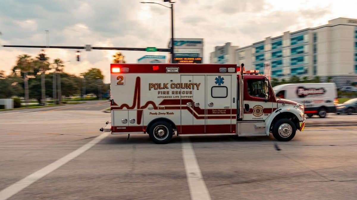 Polk County Fire Rescue Ambulance speeds through city intersection at sunset.