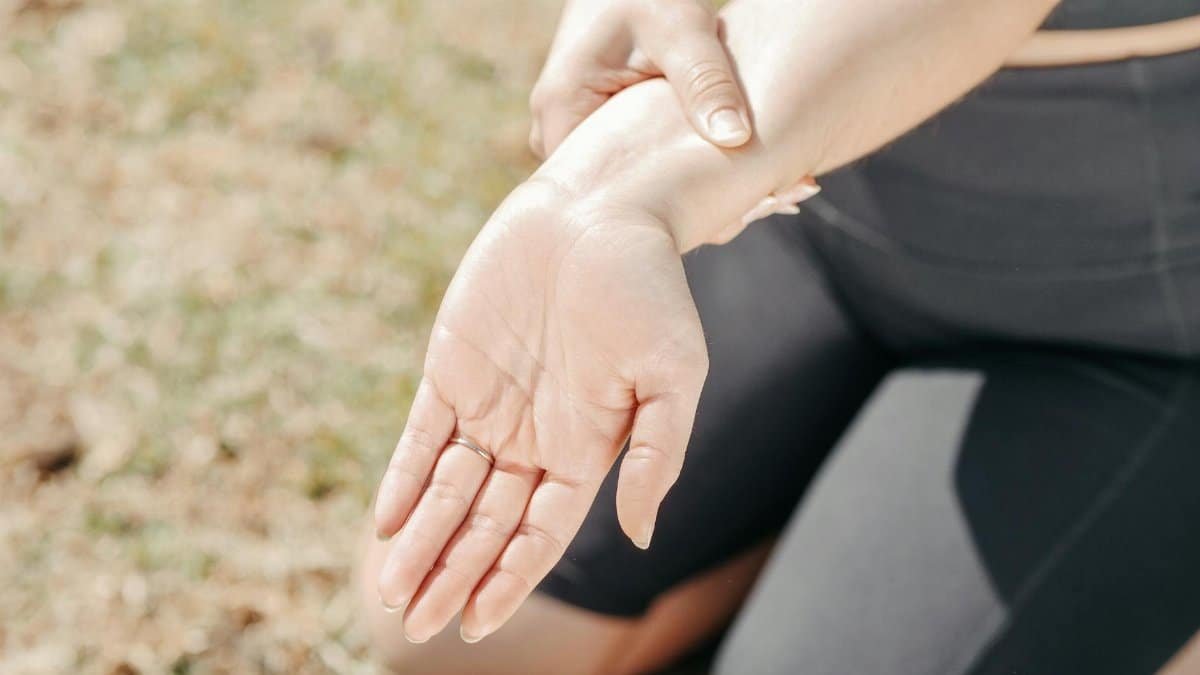 Person gripping wrist in pain, highlighting injury and support outdoors.