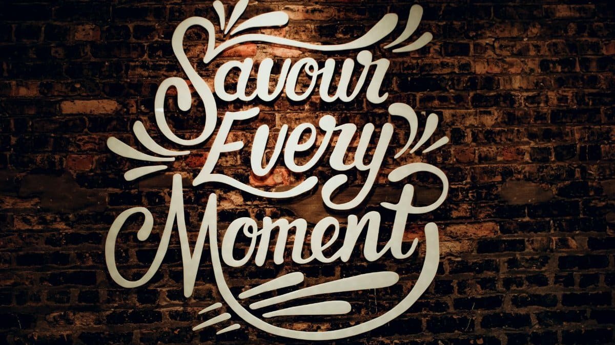 Inspirational 'Savour Every Moment' sign on a weathered brick wall with creative typography.