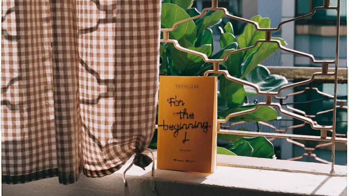 A peaceful balcony setting with book, checkered curtain, and lush plant.
