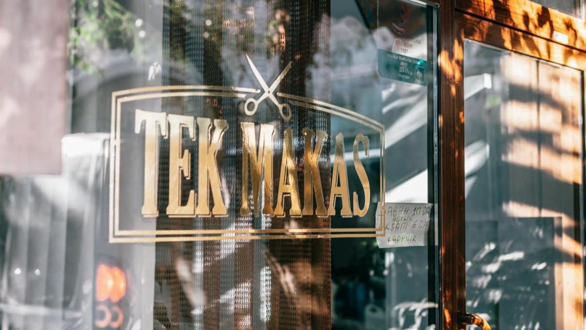 Glass wall of modern barbershop with reflection on surface and creative inscription placed near door on street in city under sunlight