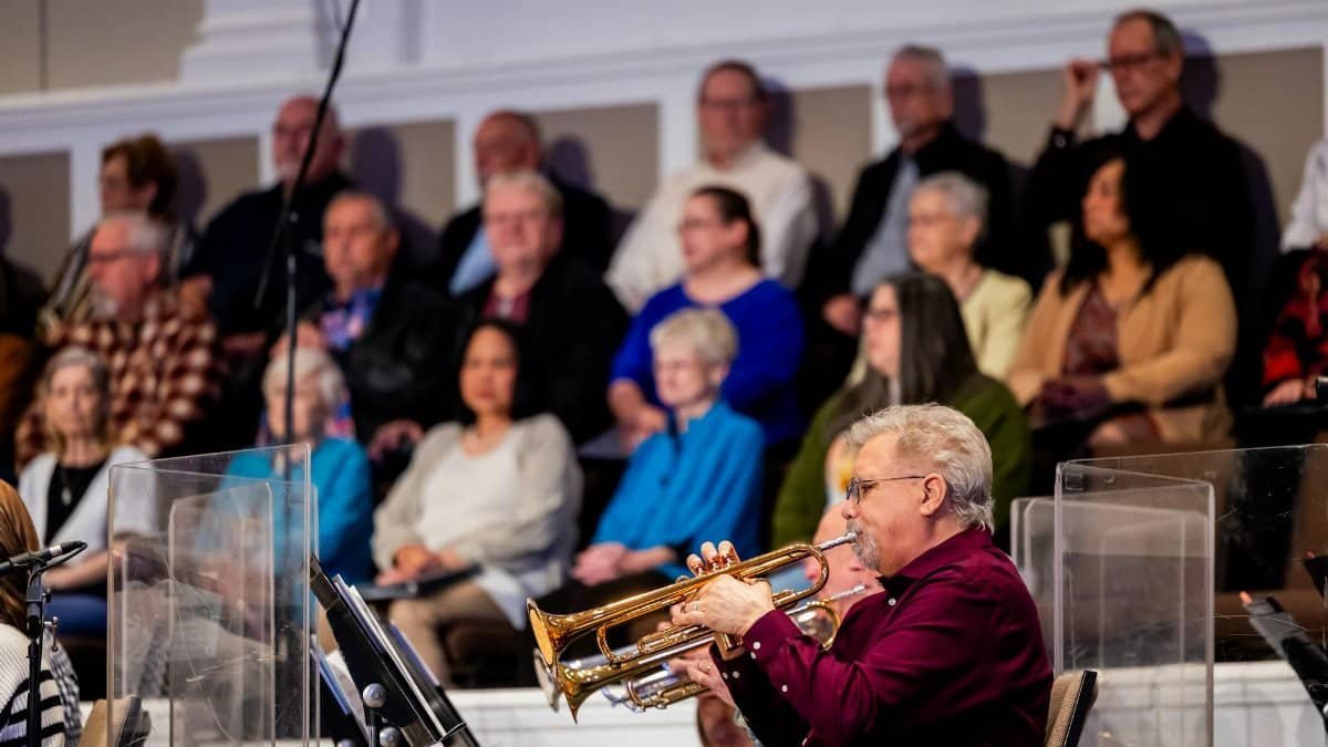 A trumpet player performs at an indoor concert surrounded by an audience, creating a lively musical atmosphere.
