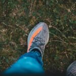 Top view of crop unrecognizable tourist in stylish footwear with stripes standing on lawn