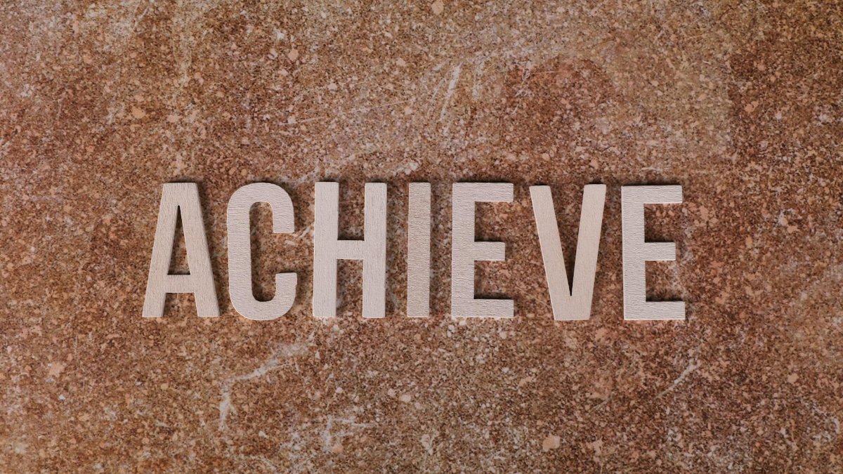 Wooden letters spelling 'ACHIEVE' on a textured brown surface, conveying motivation and success.