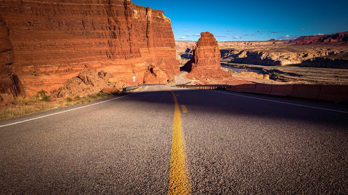 Experience the breathtaking view of a desert road cutting through Hite, Utah's stunning red rock canyons.