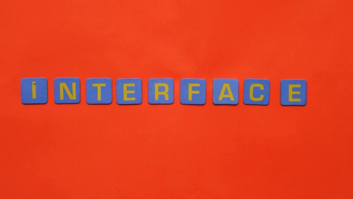 Blue blocks with yellow letters spelling 'INTERFACE' stand out against a vibrant orange backdrop.