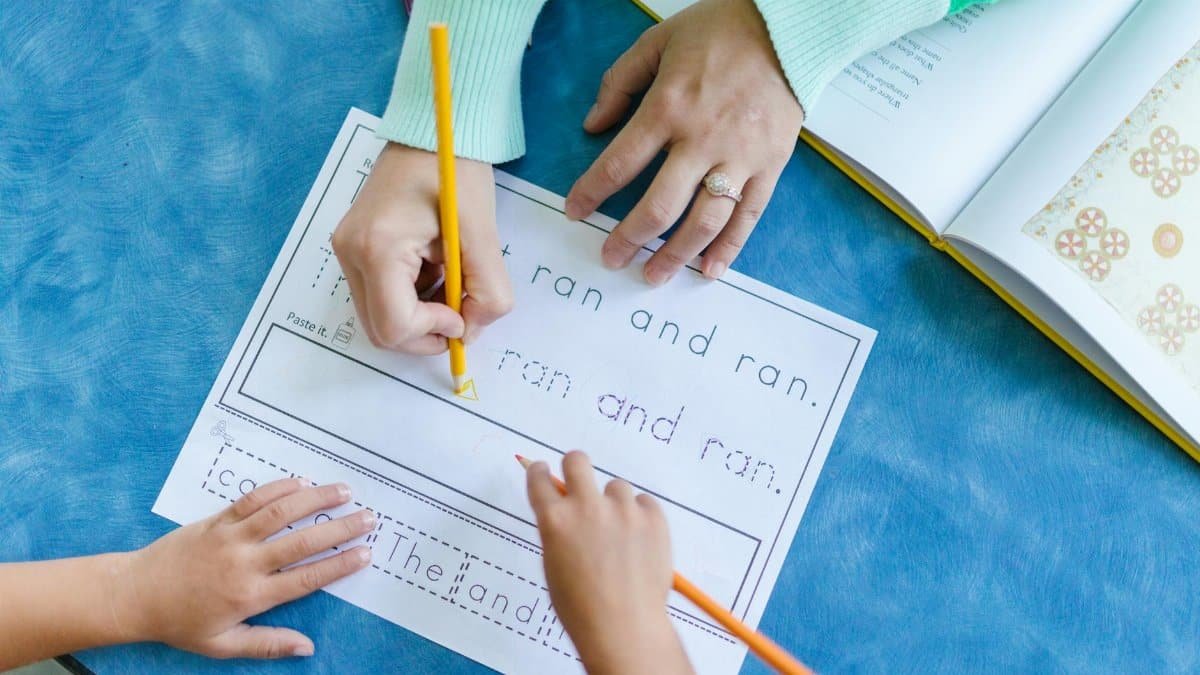 Child tracing letters with teacher guidance in a school setting.