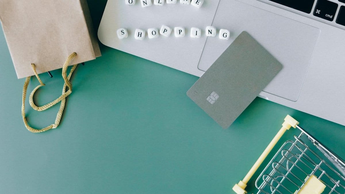 Flat lay of online shopping essentials with laptop, card, and shopping cart.