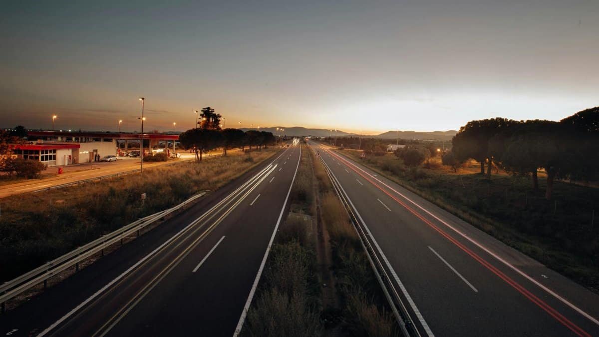A serene expressway scene captured at sunset, with long exposure light trails and a golden horizon.