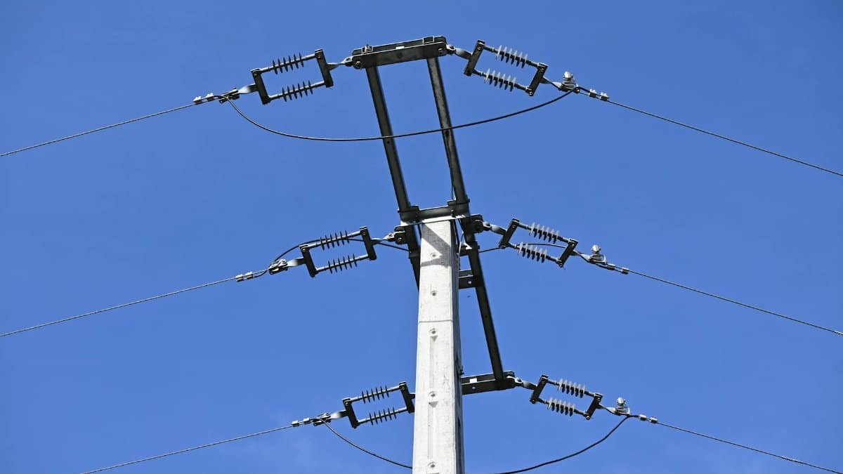 A close-up view of an electricity pole with wires against a clear blue sky, showcasing infrastructure.