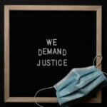 Top view arrangement of protective face mask placed on black framed image with bright white text We Demand Justice on black background