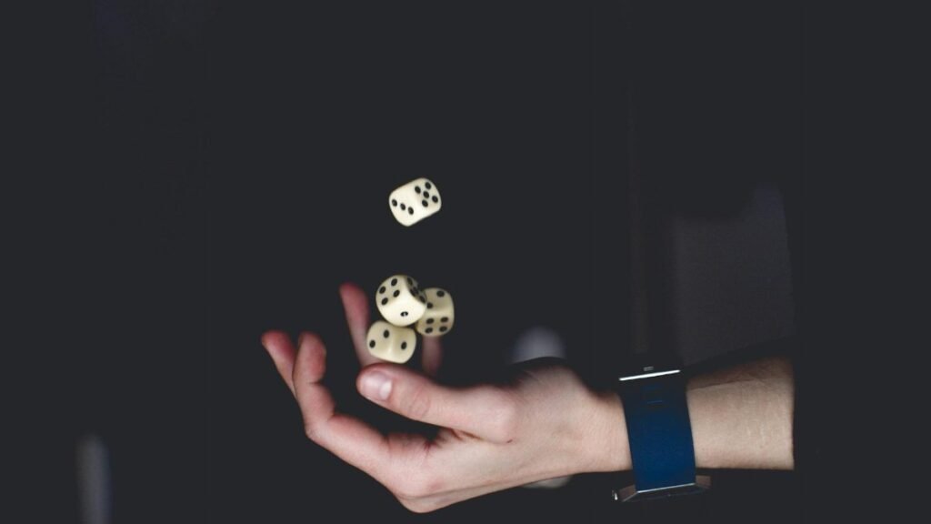 A close-up of a hand tossing several dice against a dark background, symbolizing chance and luck.