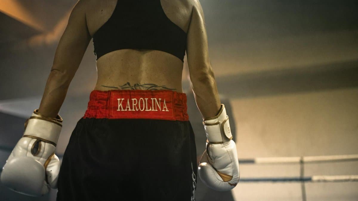 A focused female boxer preparing in the ring, wearing gloves and gym clothes, demonstrating determination.