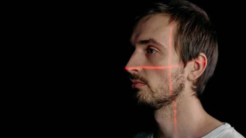 A side profile of a man with facial recognition laser scan on his face against a black background.