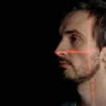 A side profile of a man with facial recognition laser scan on his face against a black background.