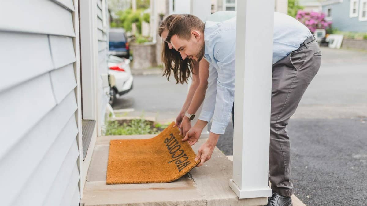 A young couple setting up a welcome mat on the porch of their new home, symbolizing new beginnings.