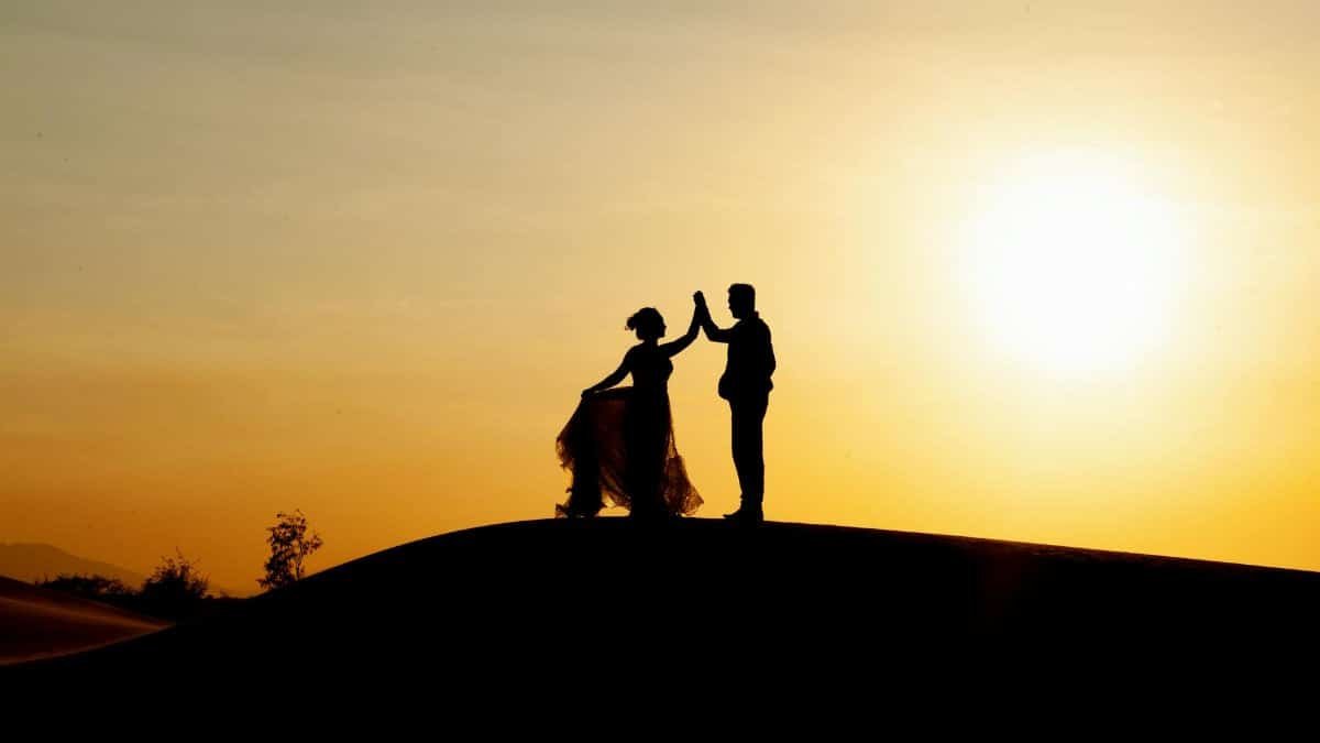 Silhouetted couple dancing on the beach during a golden sunset, creating a romantic scene.