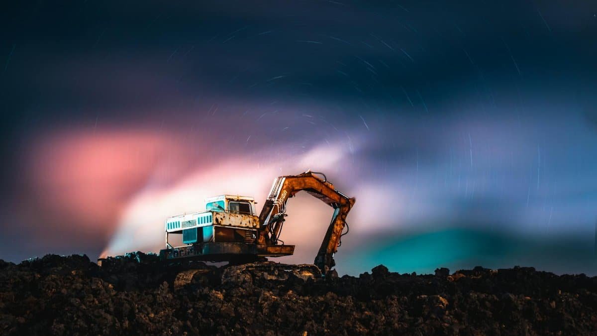 A dramatic excavator silhouette under vibrant northern lights and star trails captured at night.