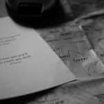 A black and white image of an inspirational travel quote alongside a map and camera lens cap.