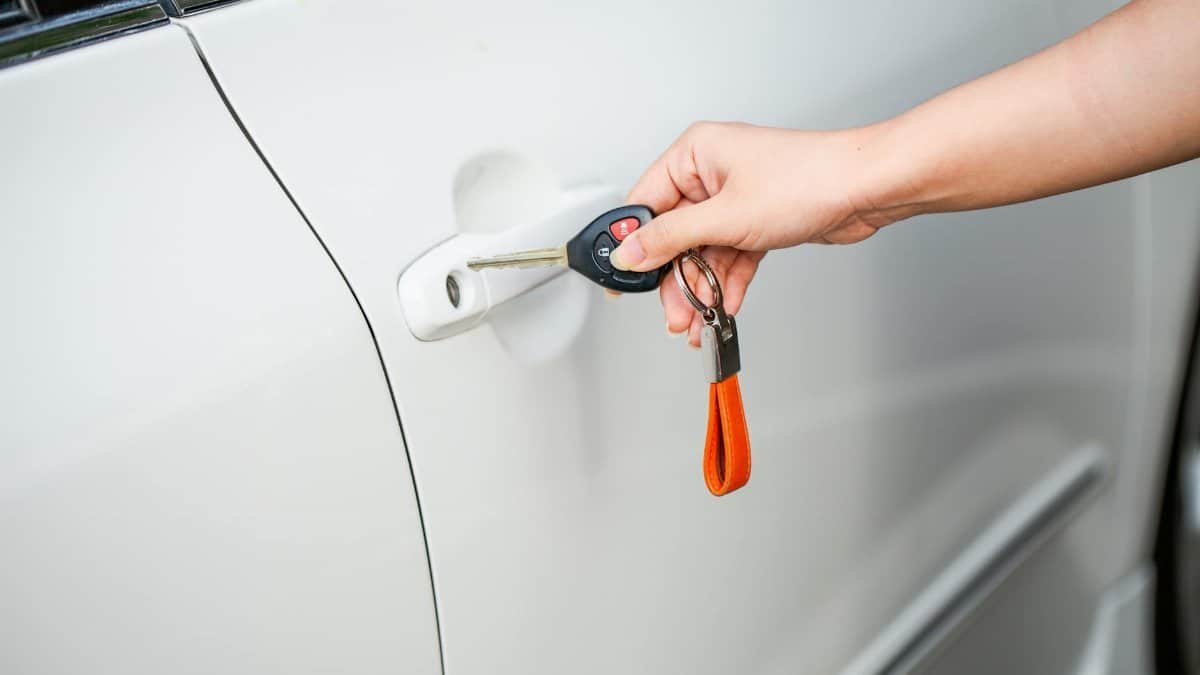 Close-up of a hand unlocking a white car door with a metal key and key fob.