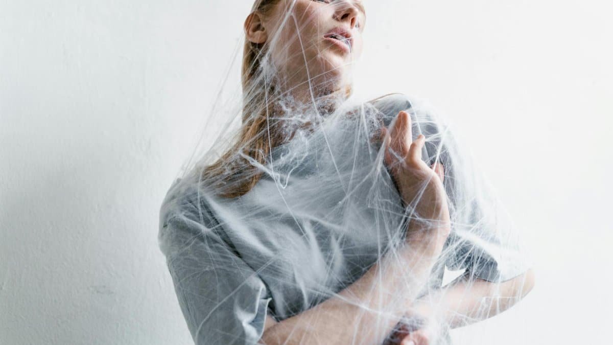 A woman enveloped in spider webs, representing anxiety and helplessness in an artistic conceptual shot.