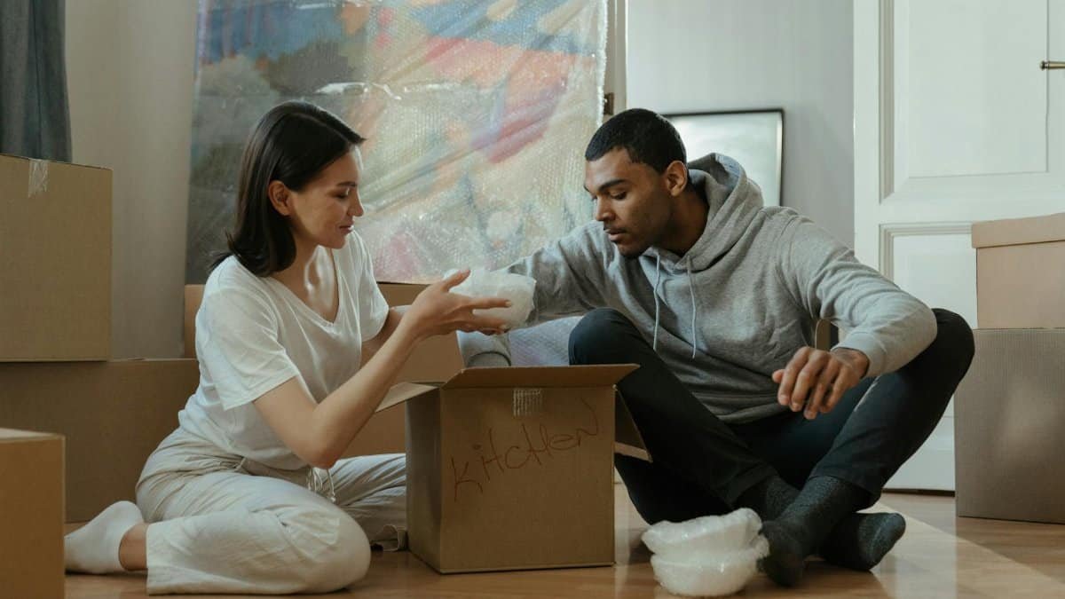 Young couple unpacking boxes in their new home, setting up kitchen items together.
