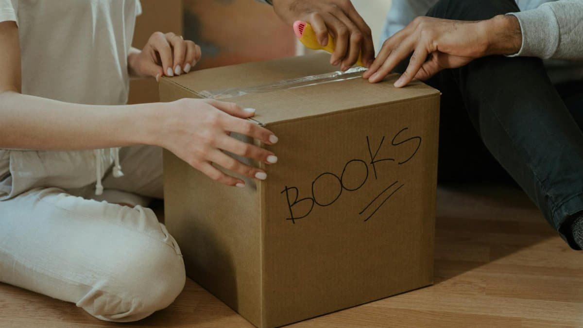 A couple unpacking books in their new home, focusing on teamwork and domestic life.