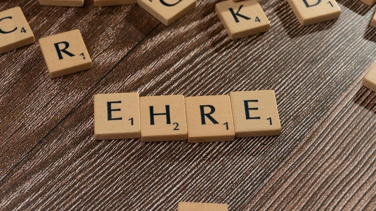 Wooden Scrabble tiles arranged to form the word 'EHRE' on a wooden surface.