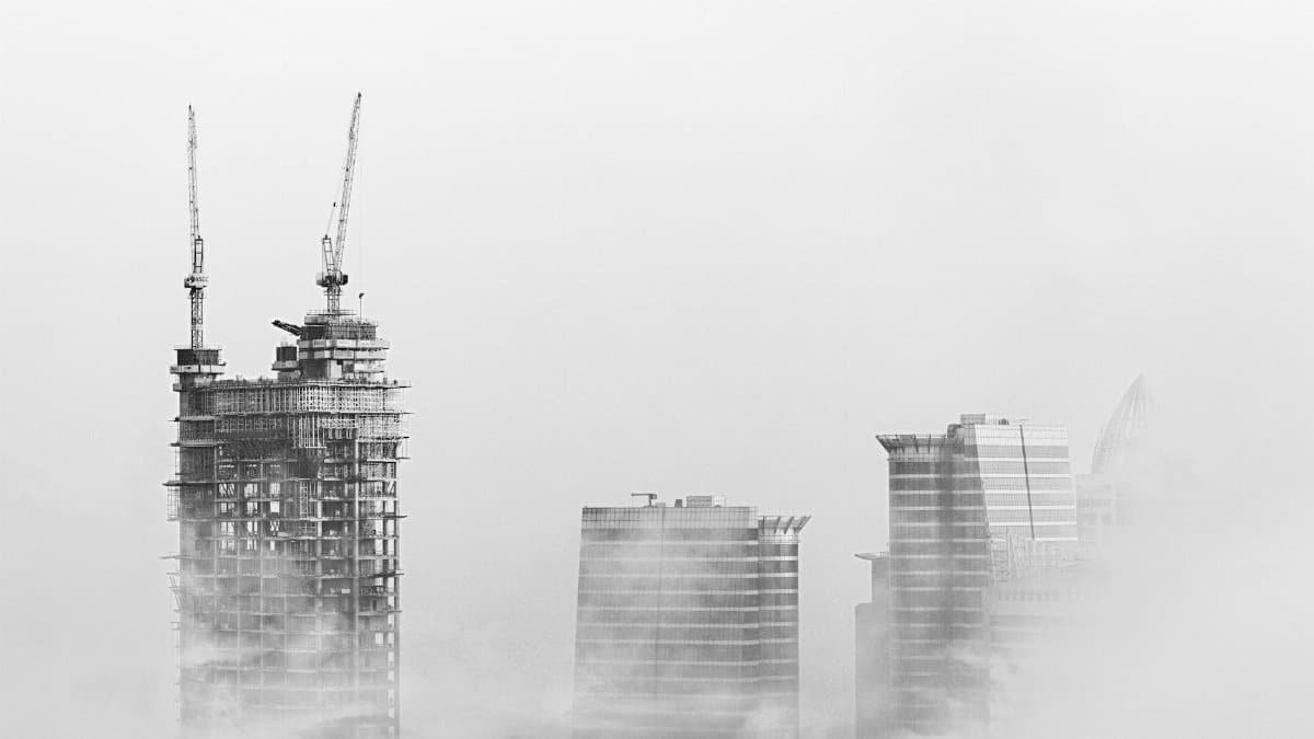 Black and white photo of Dubai skyline with skyscrapers and cranes emerging from fog, showcasing urban development.