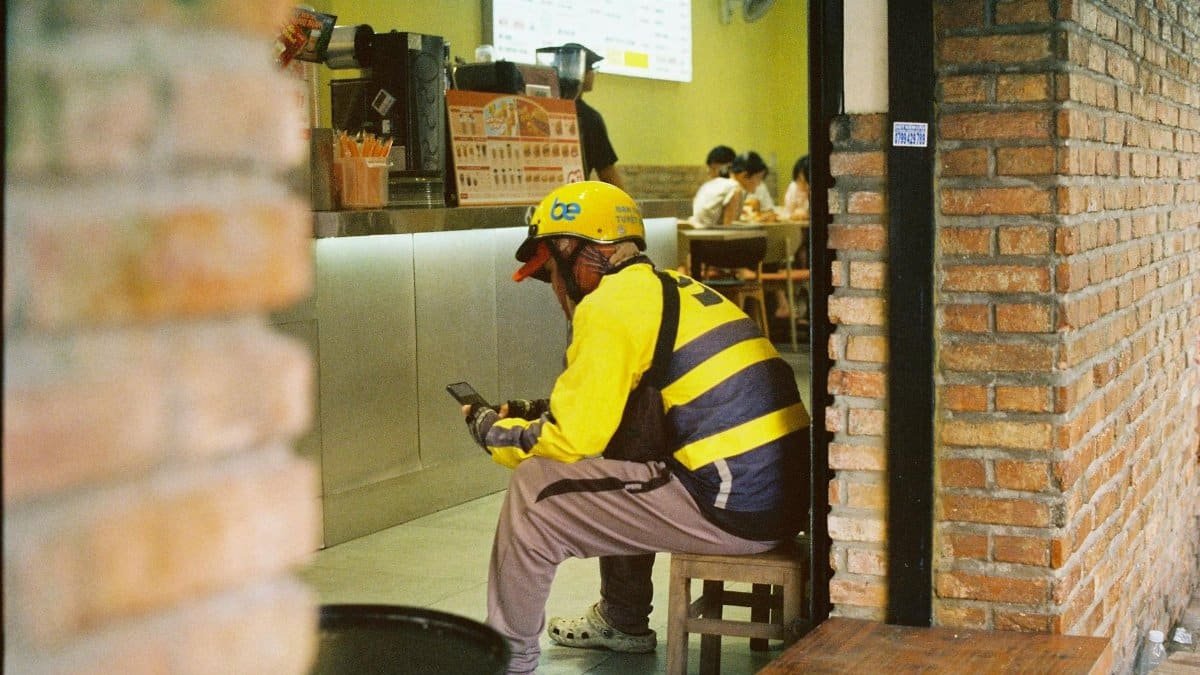 A delivery driver relaxes inside a Vietnamese cafe, engrossed in his smartphone.