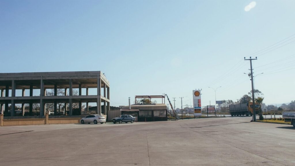 An urban gas station with empty parking spaces and visible signage under a clear sky.