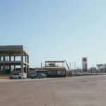 An urban gas station with empty parking spaces and visible signage under a clear sky.
