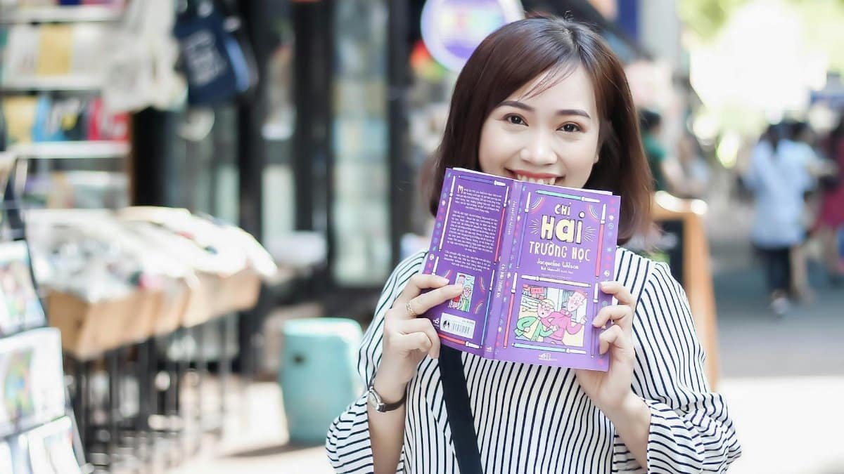 Cheerful woman reading a book in a vibrant outdoor setting, enjoying a sunny day in the city.