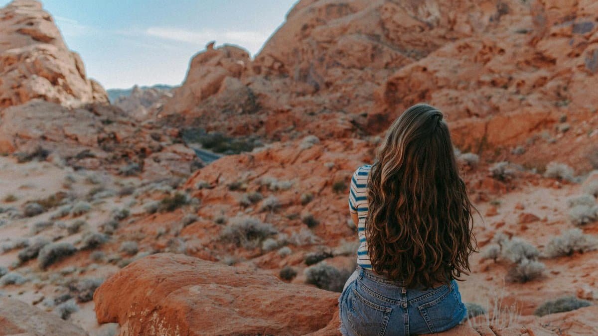 A woman sits thoughtfully on red rocks in Nevada's Valley of Fire, embracing nature's beauty.