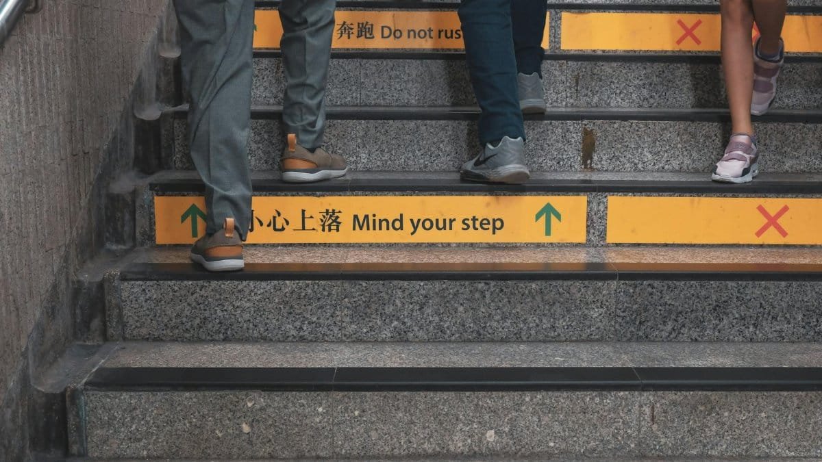 Close-up of people walking up stairs with safety signs in a subway station.