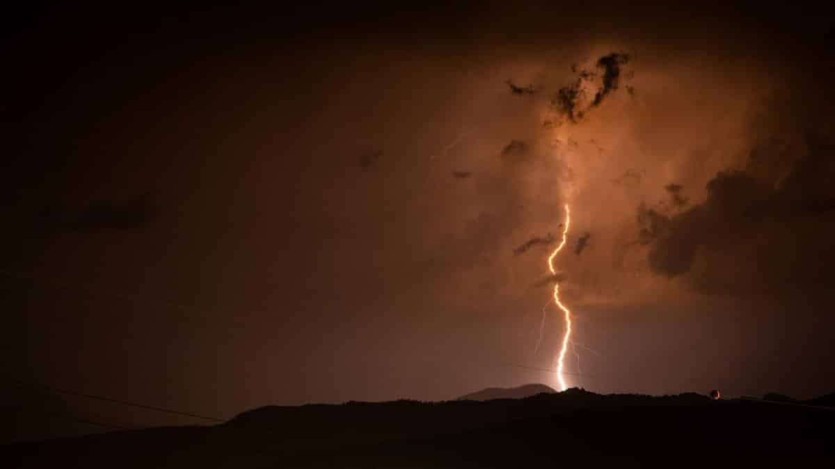 A striking bolt of lightning illuminates the night sky above silhouetted mountains during a thunderstorm.